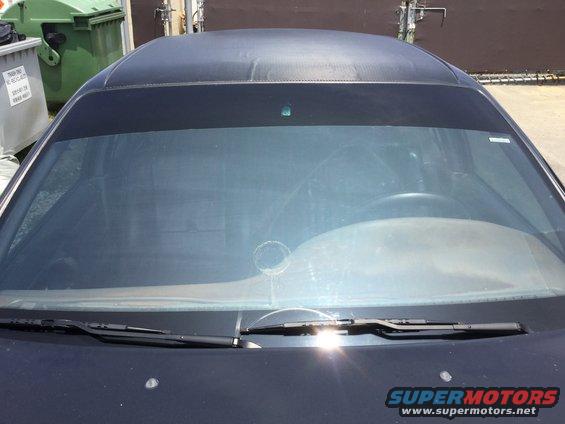 Front view of a car's windshield, dashboard, and roof. Sun glare is visible on the windshield