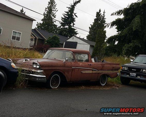 Rusty red 1957 pickup truck parked next to a dark SUV