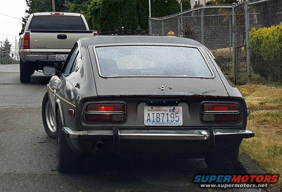 Rear view of a gray Datsun 240Z with a Washington license plate, followed by a pickup truck