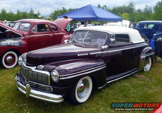 Dark purple 1947 Mercury convertible with white top and chrome trim parked on grass
