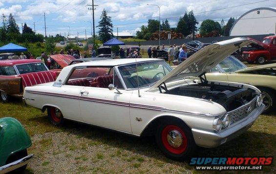 White 1961 Ford Galaxie with red interior, hood open, parked at an outdoor car show