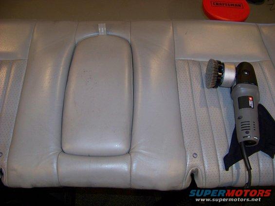 Light gray leather car seat with a center armrest and a polishing tool nearby