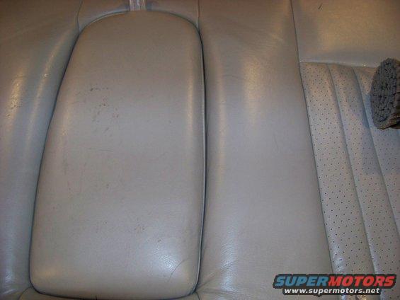 Close-up of light gray leather car seats, showing a center console armrest and perforated seat cushion