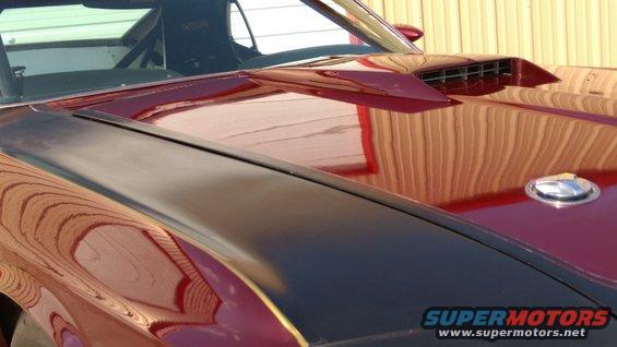 Close-up of a dark hood scoop and a chrome gas cap on a red car's hood