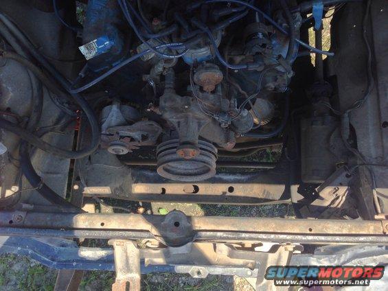 Engine bay with hoses, wires, and engine components visible. Some rust on metal parts