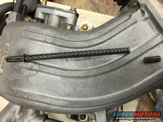 Gray engine intake manifold with a braided black cable and a hex bolt