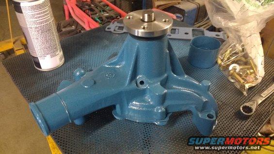 Blue water pump with metal flange on top, next to a can of spray paint and a bag of bolts