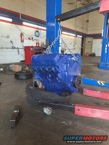 Blue engine block suspended by chains in a garage