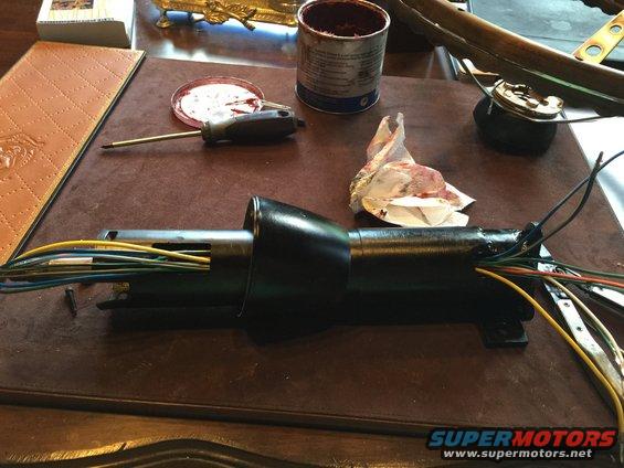 Black steering column assembly with wires on a brown surface, next to a can of grease and a screwdriver