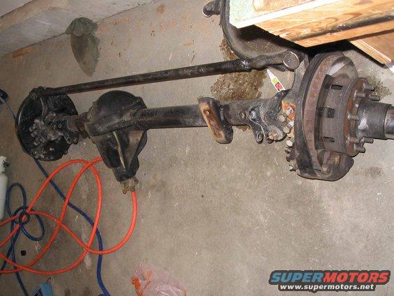 Ford Bronco front axle assembly with brake components and tie rod, on concrete floor