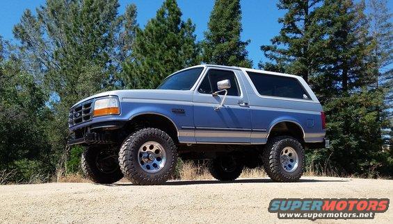 1996 Ford Bronco lifted with off-road tires, parked on a dirt road with trees in the background