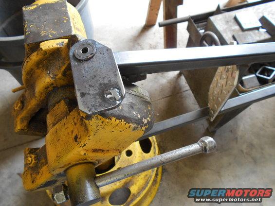 Yellow vise gripping a metal bracket attached to a steel bar