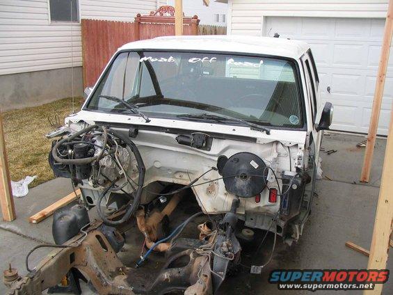 White truck body with engine removed, showing the chassis and front suspension. Text on windshield says 'Most Off Road'
