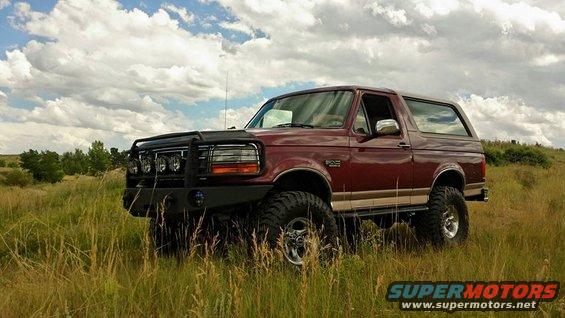 Maroon 1996 Ford Bronco with off-road bumper and lights parked in tall grass