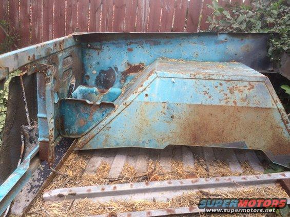 rusted blue metal car part, possibly from a truck bed or firewall area, sitting on a metal surface with straw