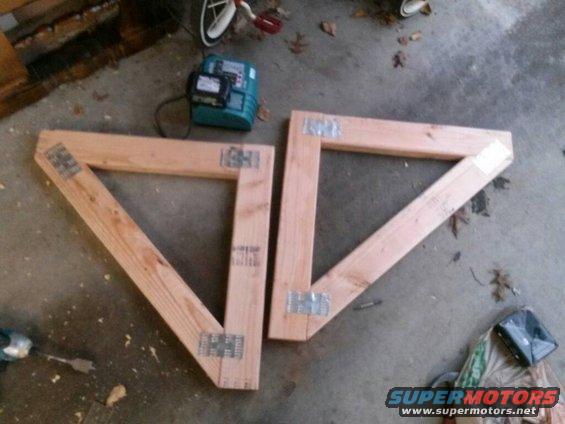 two wooden triangular frames made of lumber, joined with metal brackets, on a concrete floor