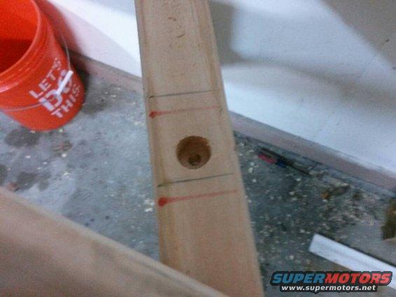 Wooden plank with a drilled hole and red markings, next to an orange bucket