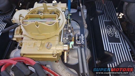 Close-up of a gold carburetor and black Ford Racing valve cover with silver stripes