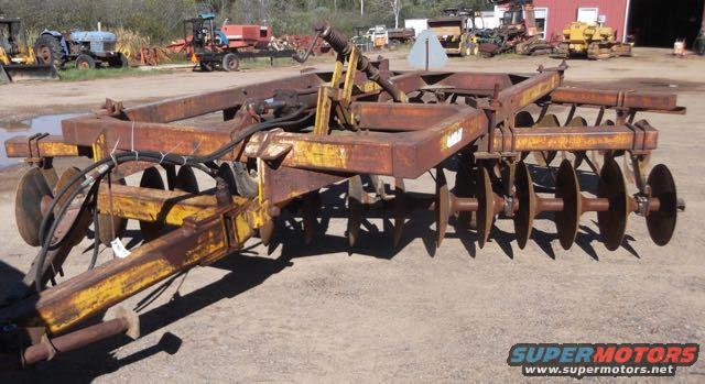 Rusty disc harrow with multiple circular blades and hydraulic hoses, angled view