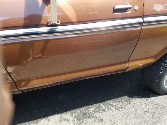 Brown 1978 Ford Bronco side door panel with chrome trim and a portion of the front tire