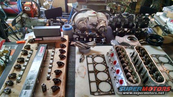Engine cylinder heads, gaskets, lifters, and other engine components laid out on a workbench