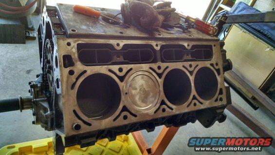 Engine block with four cylinders visible, one with a piston. Tools on top