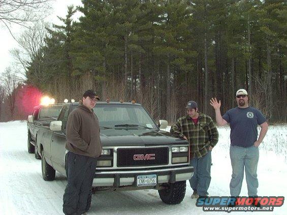 Three guys stand around a GMC pickup truck in the snow. Another truck is behind it