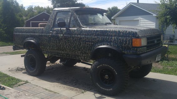 Camouflaged Ford Bronco with lifted suspension and off-road tires parked on a driveway