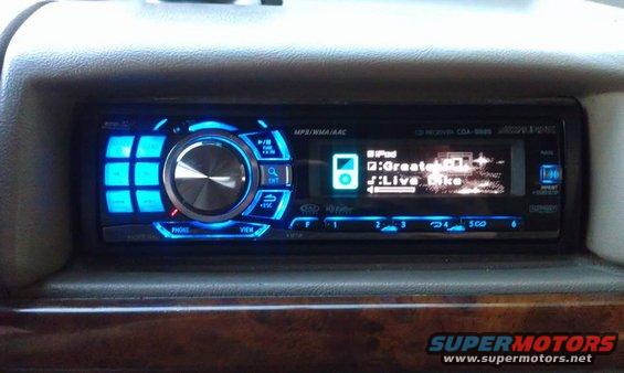 Car stereo with blue illuminated buttons and screen displaying iPod music