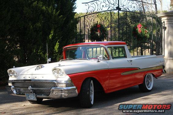Red and white 1957 Ford Ranchero parked in front of a gate with wreaths