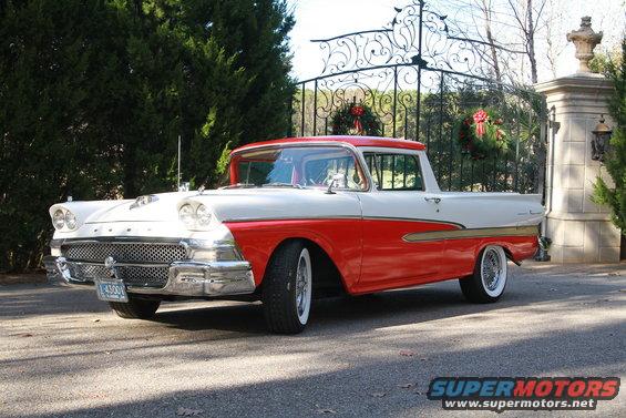 Red and white 1957 Ford Ranchero pickup truck with chrome grille and whitewall tires parked outside a gate