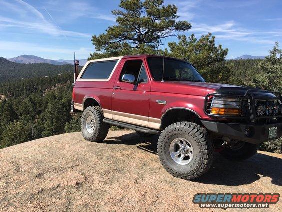 1996 Ford Bronco parked on a rocky outcrop with mountains in the background