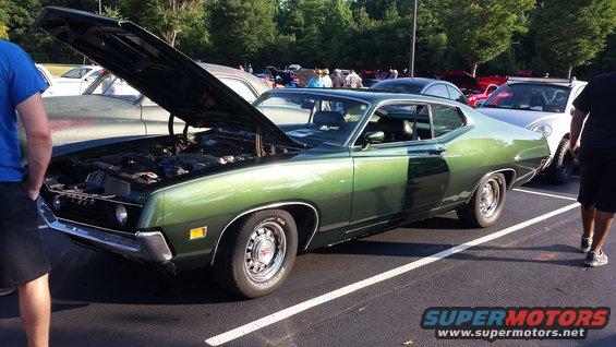 Green coupe with hood open, parked next to other cars