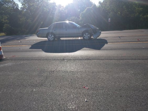 Side view of a silver sedan with severe front-end damage, stopped on the side of a road