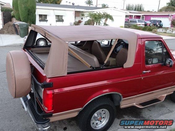 Red Ford Bronco with tan soft top, spare tire on back, tan interior