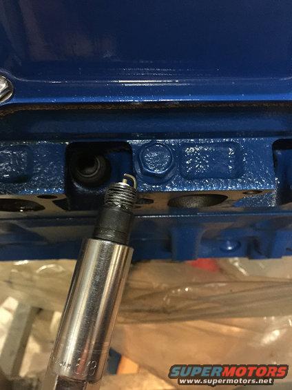 Spark plug with metal casing and threaded end, being inserted into a blue engine block