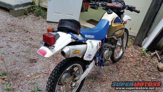 Suzuki motorcycle parked outside, showing the rear fender, exhaust, and blue seat
