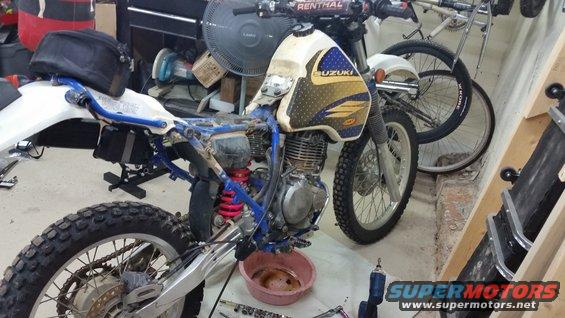 1993 Suzuki DR350S motorcycle undergoing maintenance in a workshop, with tools and a bicycle in the background