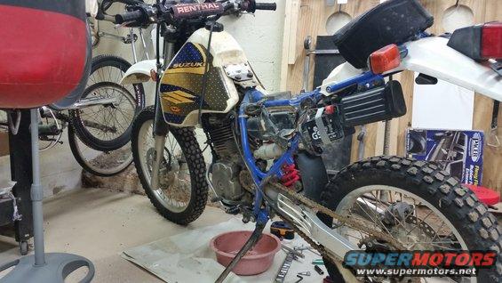 Suzuki dirt bike with parts removed, parked next to a bicycle
