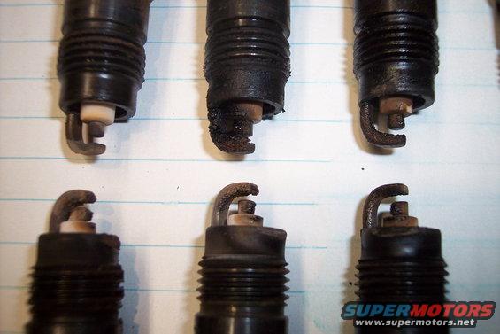Six used spark plugs, some with heavy carbon buildup, on lined paper