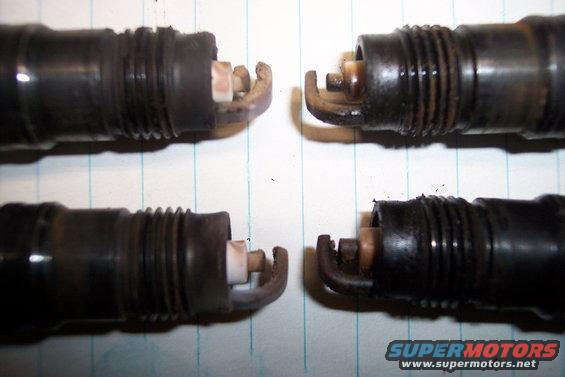 Four used spark plugs on lined paper, two in focus at top, two at bottom