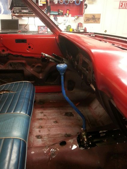 Interior view of a car with blue vinyl seats, red door panels, and a blue shifter. The floor shows signs of rust and repair