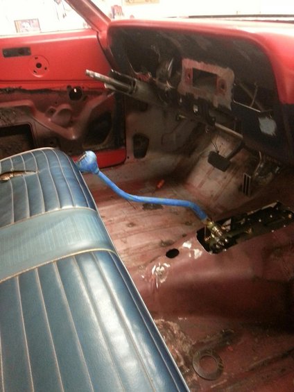 Interior shot of a car with blue bench seat, red dashboard, and a blue floor shifter. The floor is bare metal