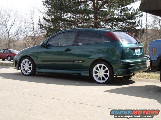 Green hatchback car with white wheels parked on asphalt, side view
