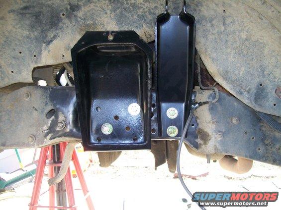 close-up of black metal brackets bolted to a vehicle's frame, with some suspension parts visible