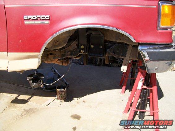 Red and tan Ford Bronco with front wheel removed, supported by jack stands