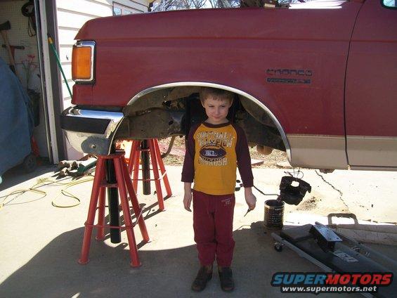 Kid standing under a red Ford Bronco that's on jack stands