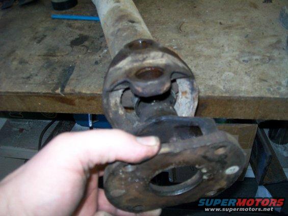 Hand holding a rusty driveshaft universal joint with a flange