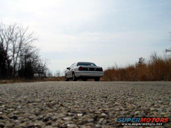 2000 Ford Crown Victoria parked on a gravel road with dry grass and trees in the background