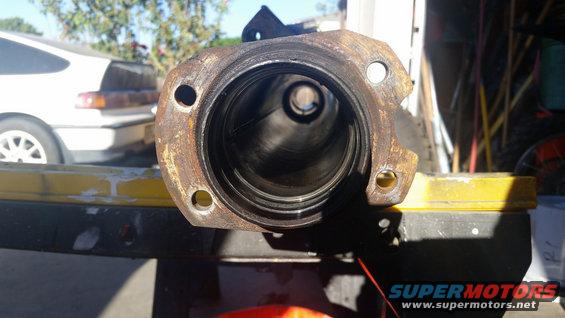 Close-up of rusty axle housing part. White car in background